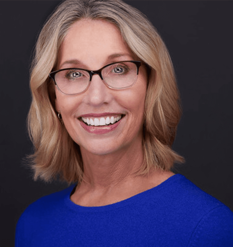 A smiling woman in glasses wearing a blue shirt.