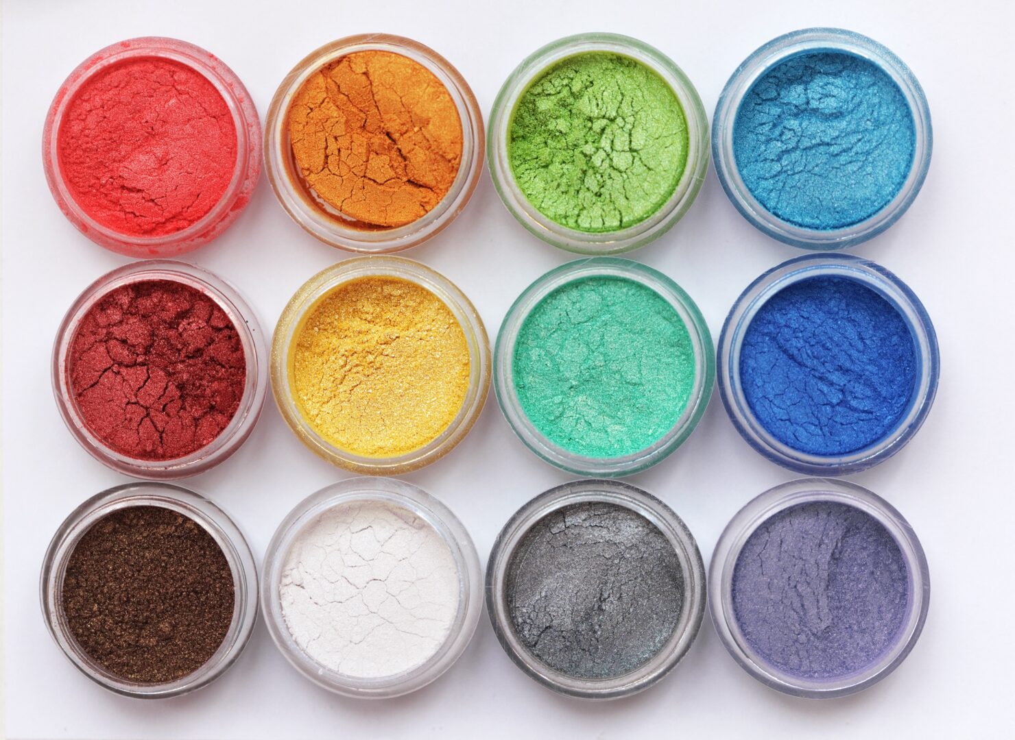 A variety of colored powders in small bowls on a white background.