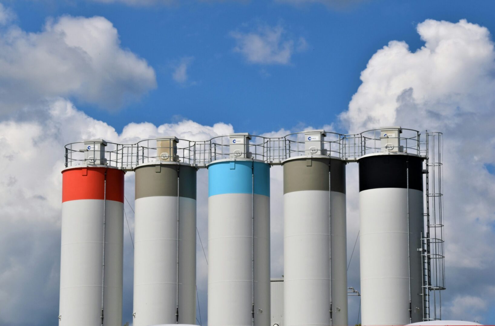 A group of white, blue, and red silos against a blue sky.