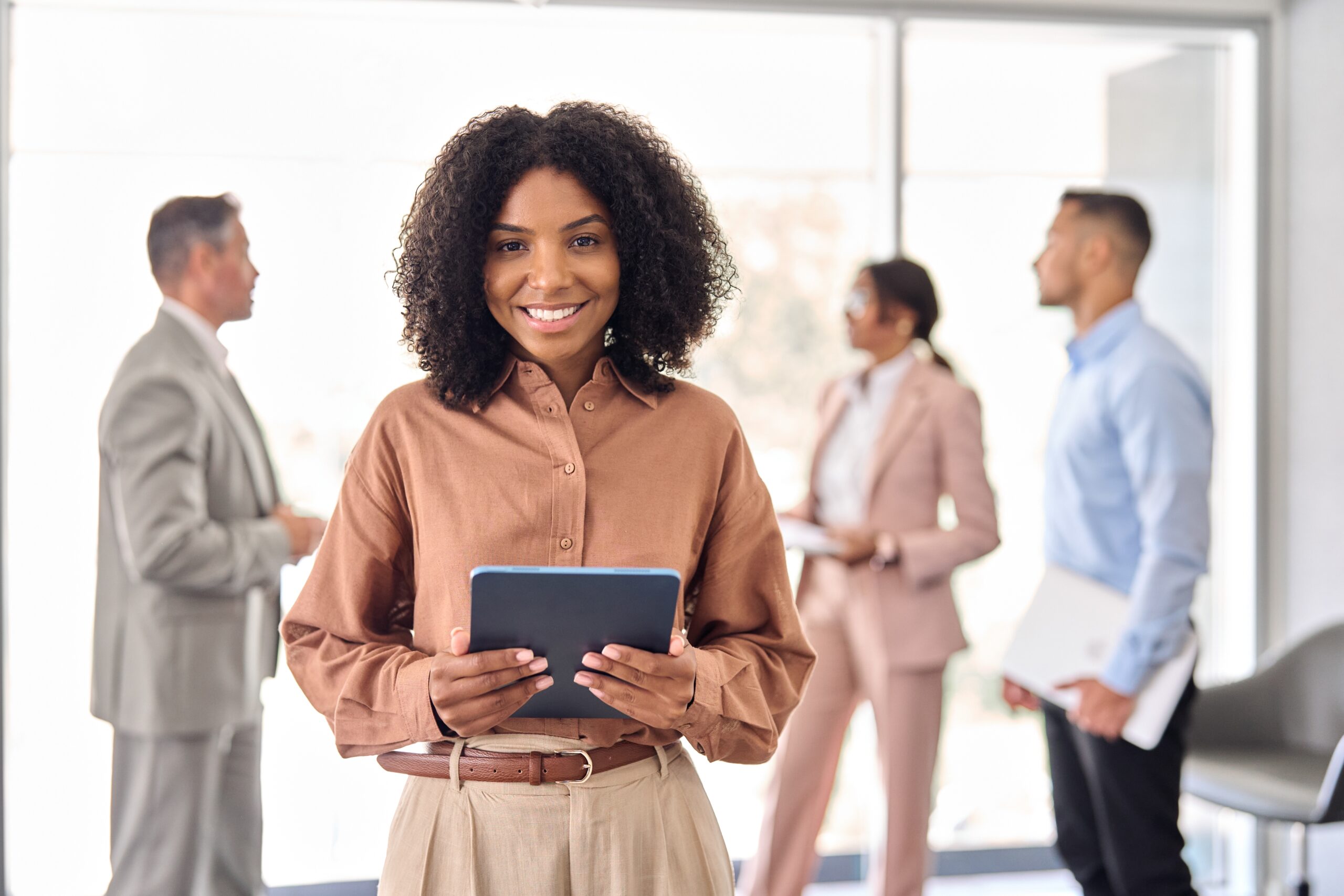 young, corporate African American woman smiles in front of her colleagues.