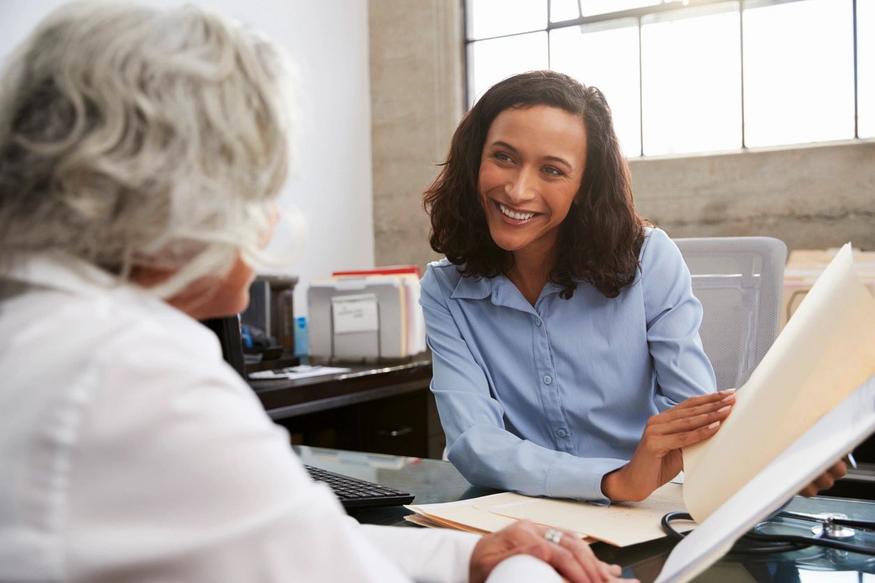 saleswoman speaking to another, older woman while sitting across a table from each other