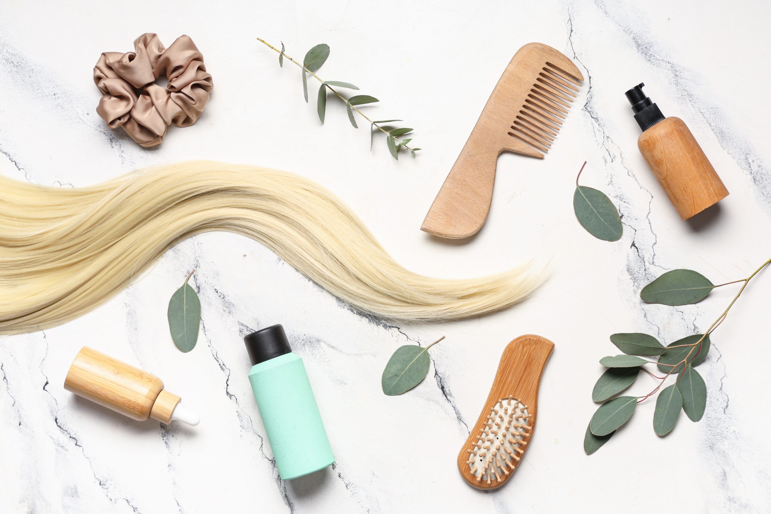 long blonde hair next to hair care products, a hair tie, and a comb