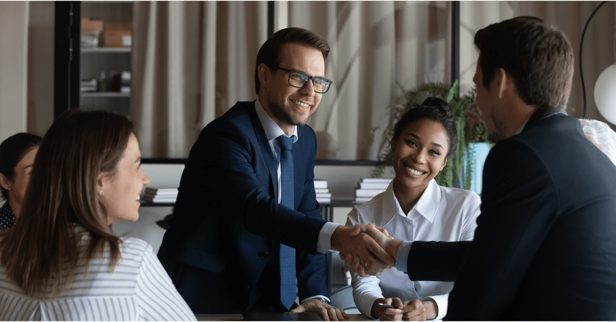 a sales account manager shaking hands after making a deal surrounded by coworkers