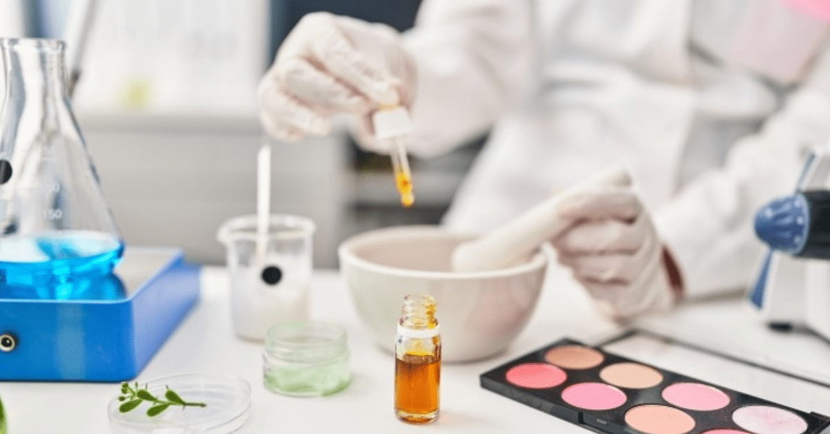 scientist dropping liquid into a mixing bowl surrounded by personal care products like cosmetics and skincare