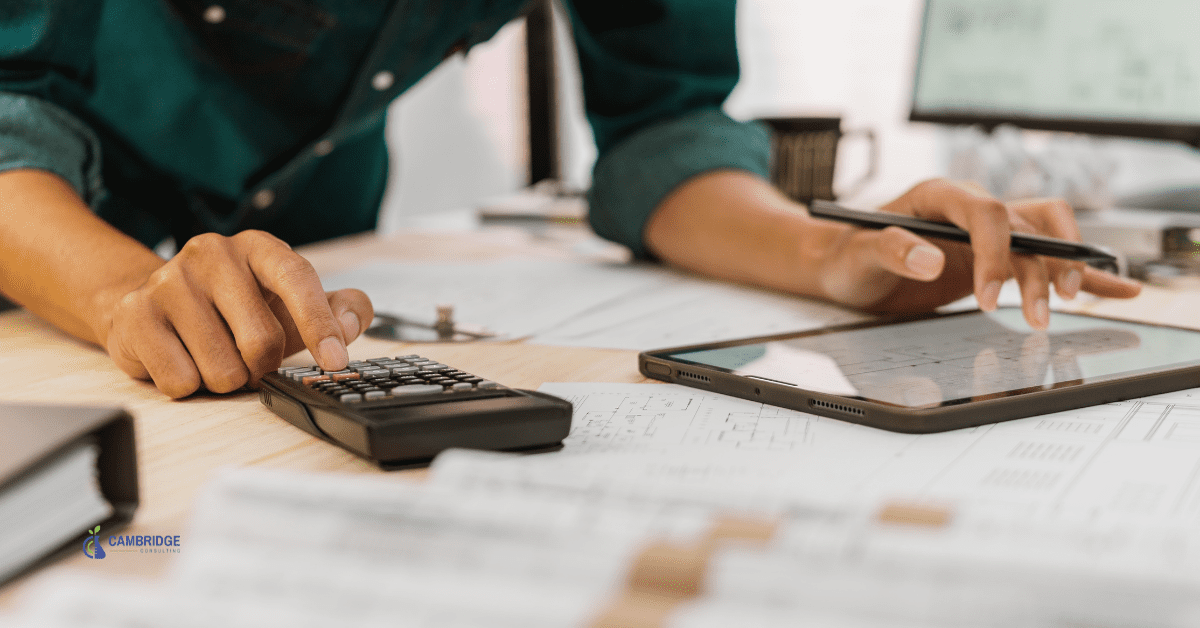 a man working on a desk typing onto a calculator and looking at a smart tablet