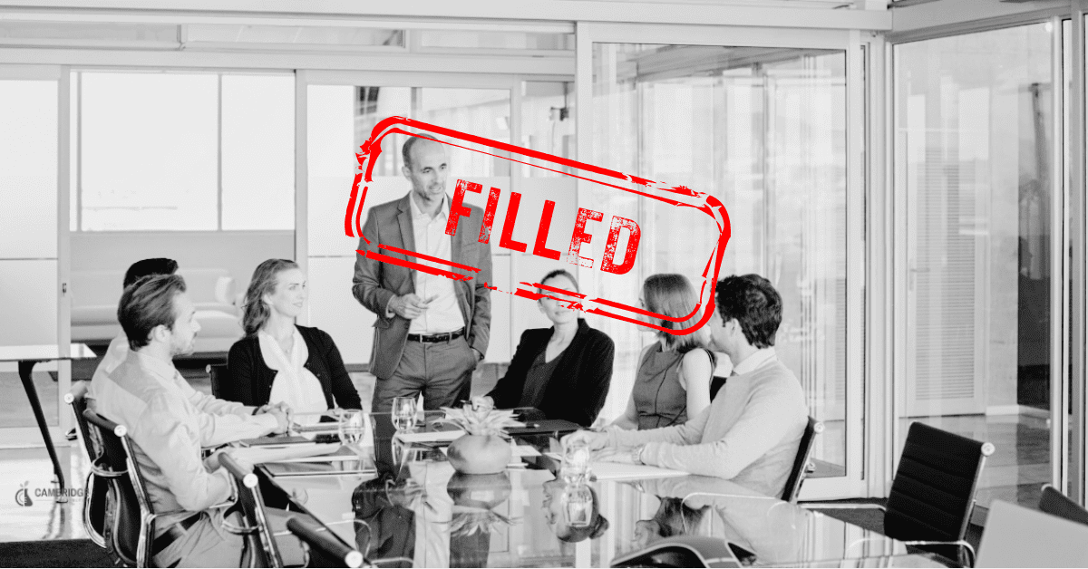 A black and white image of a group of corporate workers surrounding a conference table in a meeting room with a red stamp overlay saying "filled."