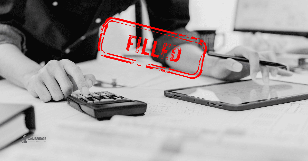 Black and white image of a corporate man typing into a calculator and spreadsheet with a red stamp overlay saying "filled" in reference to the job listing