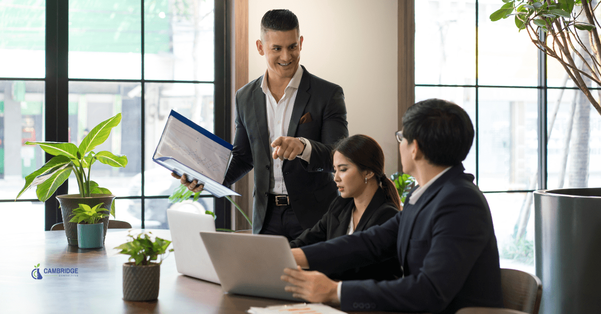 corporate team meeting with three people, one man standing giving a presentation to two colleagues