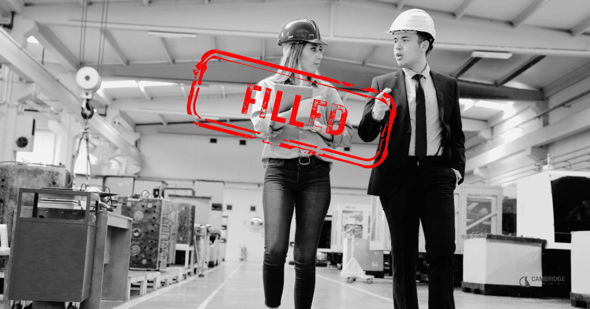 black and white image of two coworkers walking through a manufacturing plant with a red stamp overlay that says "filled".