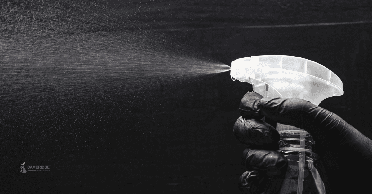 white and black image of someone spraying a cleaning bottle wearing a protective glove