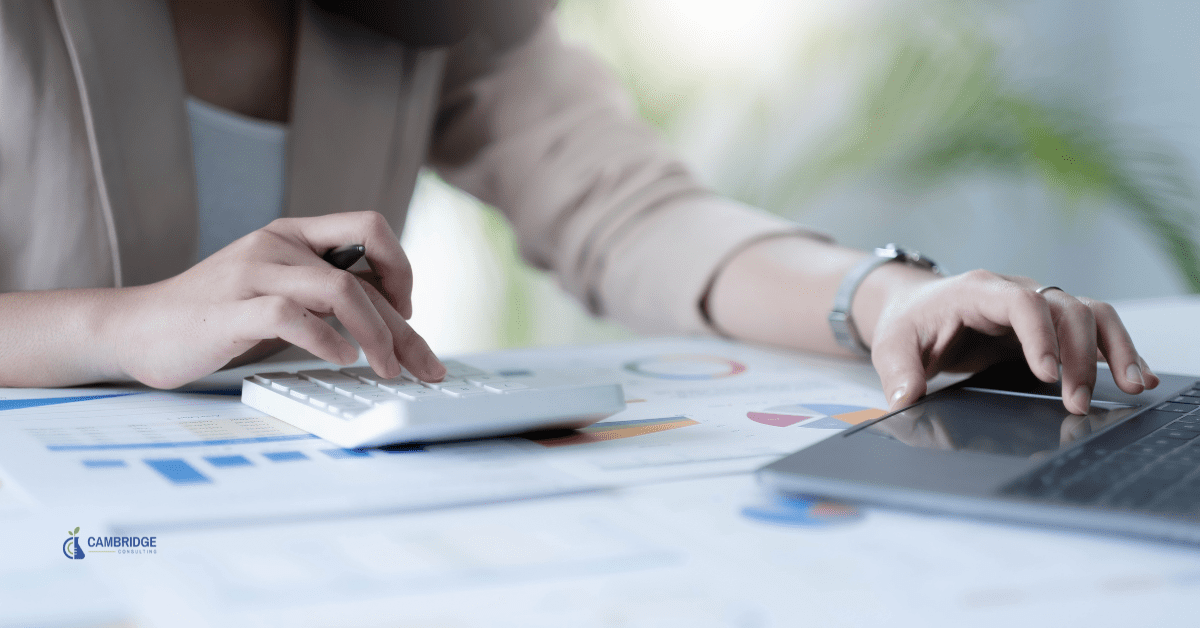 a corporate woman managing financial spreadsheets at her desk typing numbers into a calculator and onto a laptop