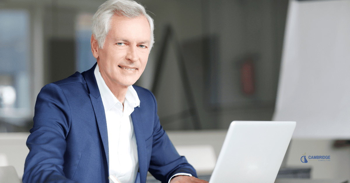 a corporate man smiling at his desk working in front of his laptop