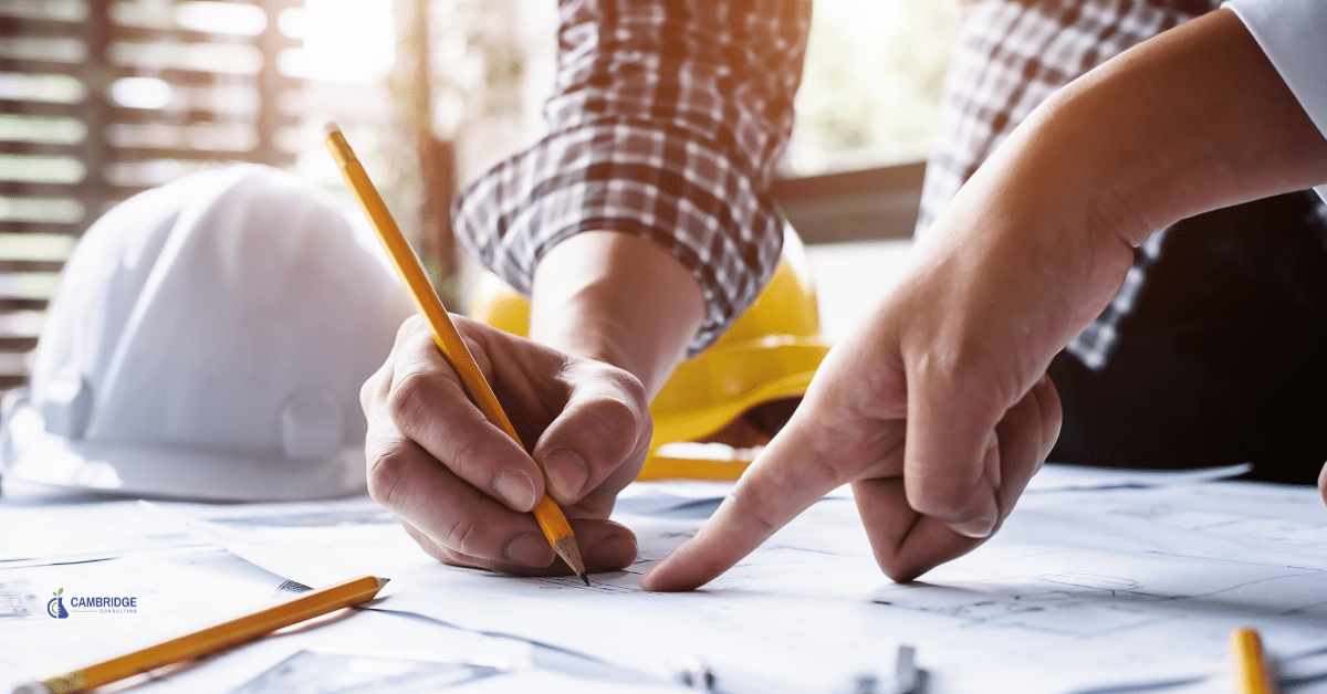 Man standing over a desk holding a pencil writing project plans