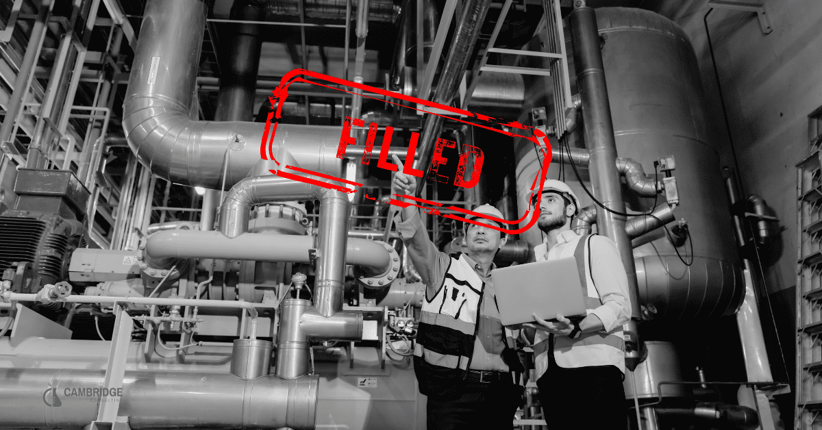 a black and white image with a red stamp overlay that says FILLED. The image is of two men working in a manufacturing plant.